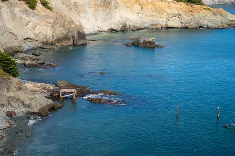 Broken down dock on cliffside leading to body of water Stock Photos