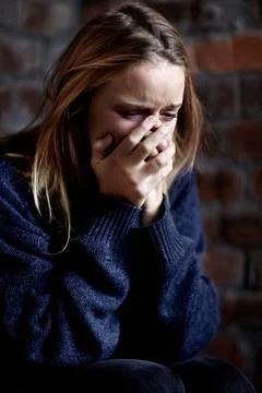 Broken down emotionally. Abused young woman crying hard and covering her mouth. Stock Photos