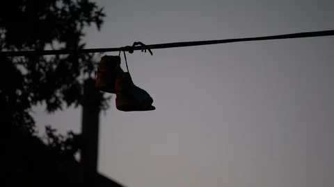 A broken down pair of sneakers tied to power lines with trees in the Vídeo Stock 115911801