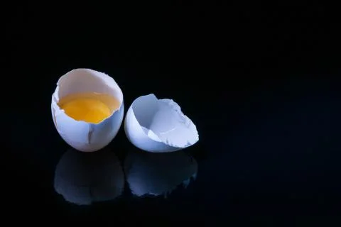 Broken egg on a black surface and black background. Stock Photos