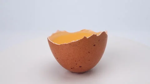 Broken egg in half eggshell is turning on white background. close up of egg yolk Stock Footage 248435322
