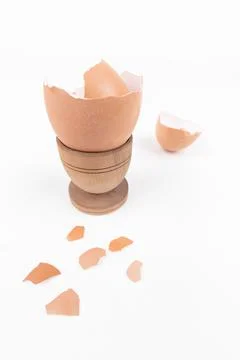 Broken egg shell in old wooden eg stand and scattered across white surface Stock Photos