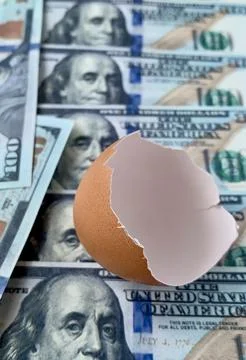 A broken egg shell rests amid a layered arrangement of hundred dollar bills, 스톡 사진