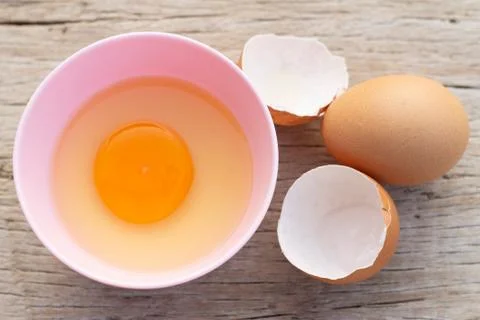 Broken egg shells and eggs on bowl, raw egg in small bowl at wooden backgroun Stock Photos