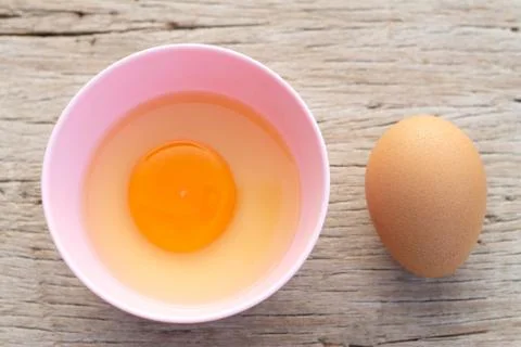 Broken egg shells and raw egg in small bowl  at wooden background for menu an Foto stock