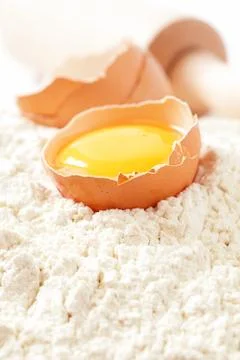 Broken egg with shells on flour, white backdrop Stock Photos