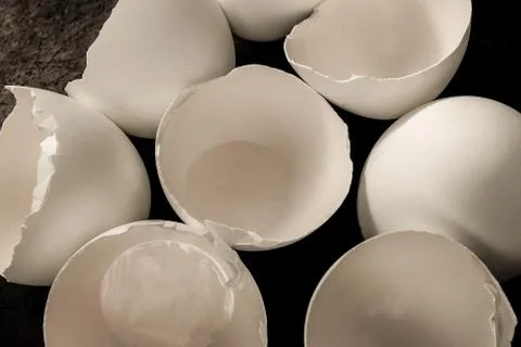 Broken eggs close up image. Shell fragments or shatters on black kitchen tabl Photos