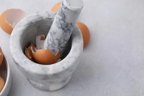 Broken eggshells, mortar and pestle on grey table, closeup. Space for text Foto stock