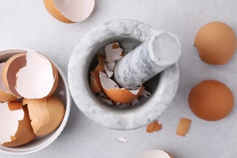 Broken eggshells, mortar and pestle on grey table, flat lay Foto stock
