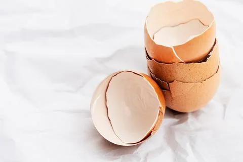 Broken eggshells stacked with a half shell on crumpled paper, copy space. Stock Photos