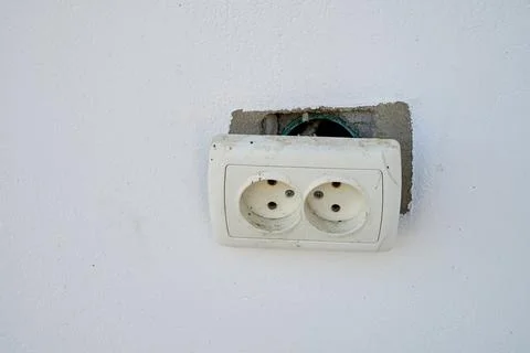Broken electrical socket on a white wall. Stock Photos