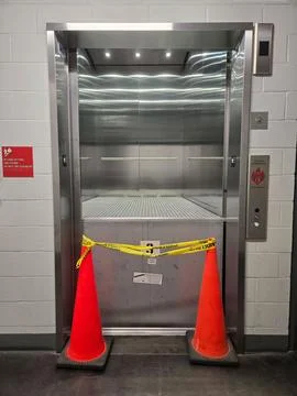 Broken elevator stopped halfway to floor with doors open and caution tape. Stock Photos