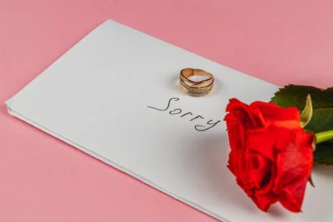 Broken engagement ring and red rose with a sorry note on a pastel background Stock Photos