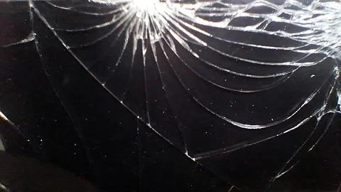 Broken glass screen showing sharp spiderweb cracks on black surface Stock Photos