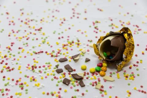 Broken golden chocolate easter eggs with colorful chocolates inside on white  Stock Photos