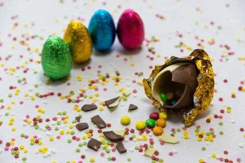 Broken golden chocolate easter eggs with colorful chocolates inside on white  Stock Photos