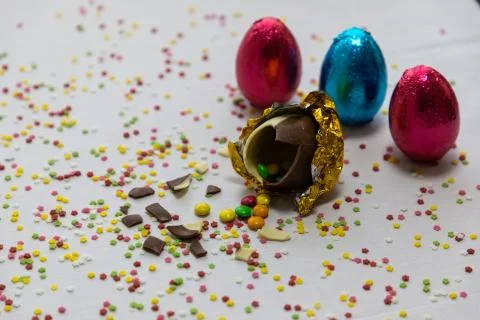 Broken golden chocolate easter eggs with colorful chocolates inside on white  Stock Photos