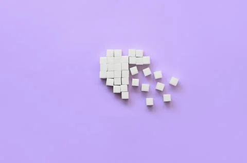 A broken heart made of sugar cubes lies on a trendy pastel violet background Stock Photos
