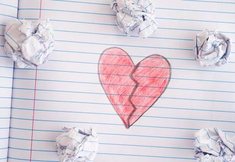 Broken Heart on notebook sheet with some crumpled paper balls on it Stock Photos