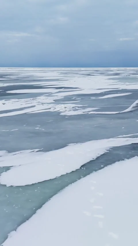 Broken ice slabs on the shore with a wide frozen sea and scattered snow patches Stock Footage 333655812