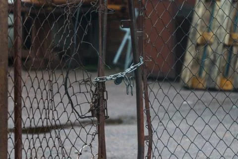 Broken mesh gate with a lock and chain on an old abandoned warehouse Stock Photos