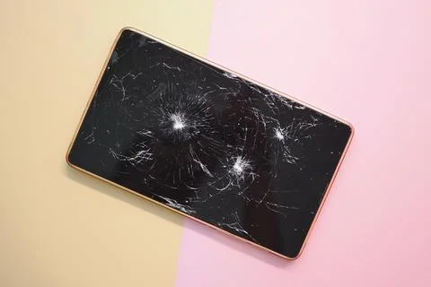 Broken mobile phone lying on a colored surface with visible cracks Stock Photos