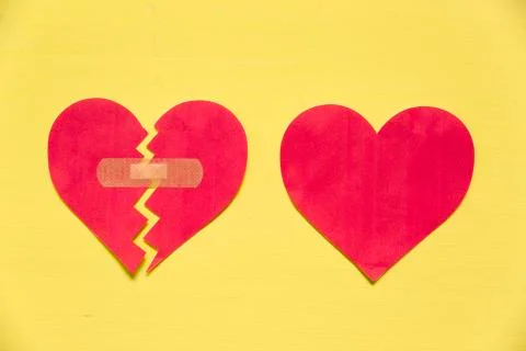 Broken paper heart with patch next to the whole paper heart on yellow backgro Stock Photos