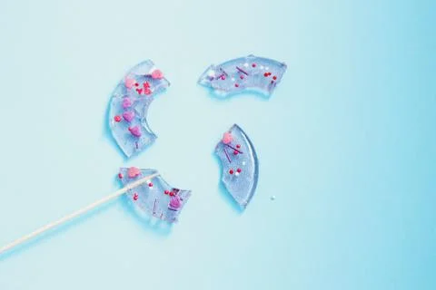 Broken in pieces candy on a stick. Smashed lollipop on blue background. Top v Stock Photos