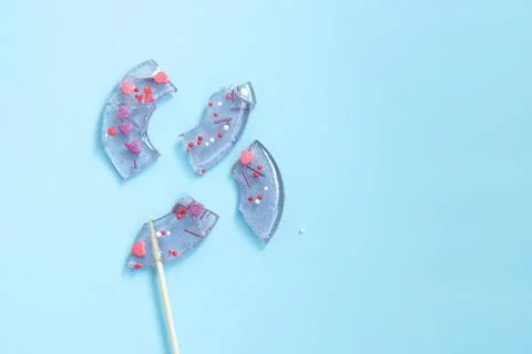Broken in pieces candy on a stick. Smashed lollipop on blue background. Top v Stock Photos