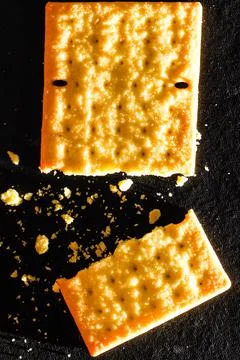 Broken Pieces of Crispy Wheat Cracker with Scattered Crumbs on Black Backgr.. Fotos de archivo