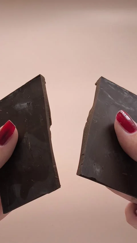 Broken pieces of dark chocolate from cocoa beans in a womans hand on a pink Stock Footage 324554696