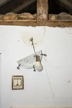 Broken plastic light switch and hanging light bulb ripped from a white wall.. Photos