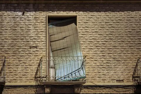 Broken plastic window roller shutter hangs crookedly over a small metal balco Stock Photos