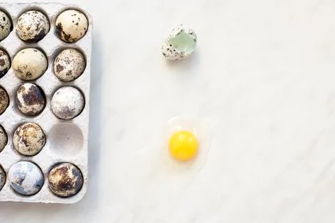 Broken quail egg on a marble surface and a cardboard box with eggs Stock Photos