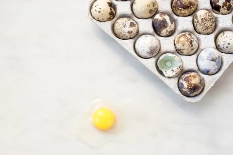 Broken quail egg on a marble surface and a cardboard box with eggs Stock Photos