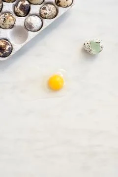 Broken quail egg on a marble surface and a cardboard box with eggs Stock Photos
