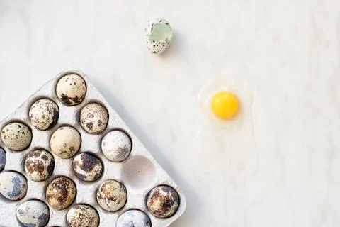 Broken quail egg on a marble surface and a cardboard box with eggs Stock Photos