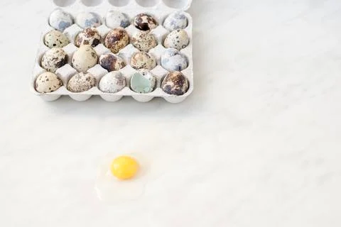 Broken quail egg on a marble surface and a cardboard box with eggs Stock Photos