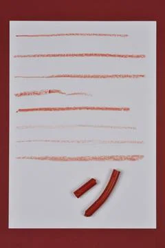 Broken red crayon with drawn lines on white paper Stock Photos