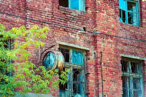 A broken round clock on an abandoned brick building. Arrow at 12 o'clock. Stock Photos