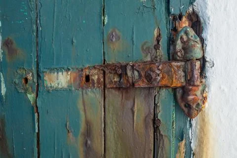 A broken rusting door hinge on a painted wooden door, paint peeling off the wood Stock Photos