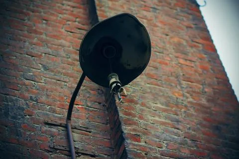 A broken rusty old lantern hangs on the wall of an abandoned brick house aban Stock Photos