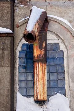 Broken rusty pipe in the red brick wall of an abandoned old factory building Stock Photos