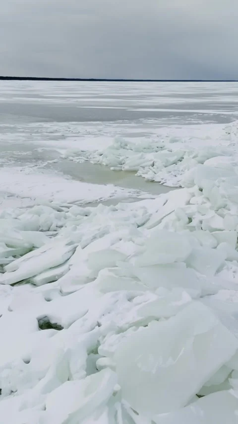 Broken sea-ice slabs piled along a frozen bay beside a pale green meltwater Stock Footage 332456347