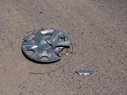 A broken silver plastic cap on the rim of a car wheel thrown on the road. Stock-Fotos