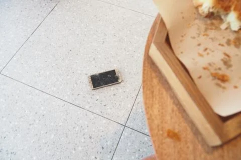 Broken Smartphone lying on the floor next to a wooden table Stock Photos