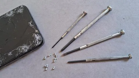 Broken smartphone screen lying next to small metal precision screwdrivers Stock Photos