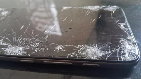 Broken smartphone screen with multiple cracks on a dark surface Foto stock