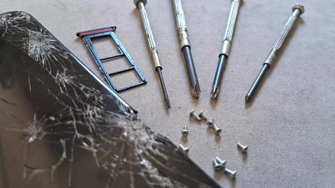 Broken smartphone screen with precision repair tools and small metal screws Stock Photos