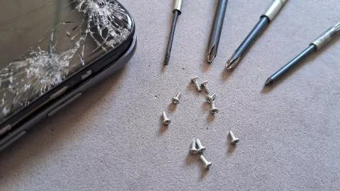 Broken smartphone screen with small metal screws and precision repair tools Stock Photos